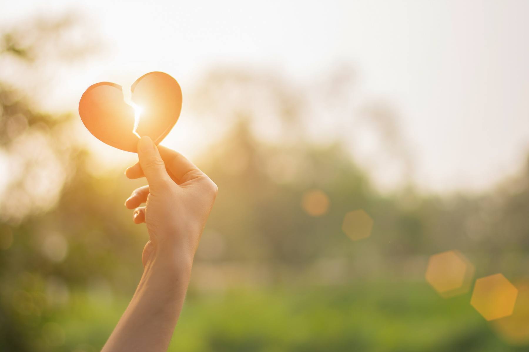 Female hand holding up a broken heart with blurred background