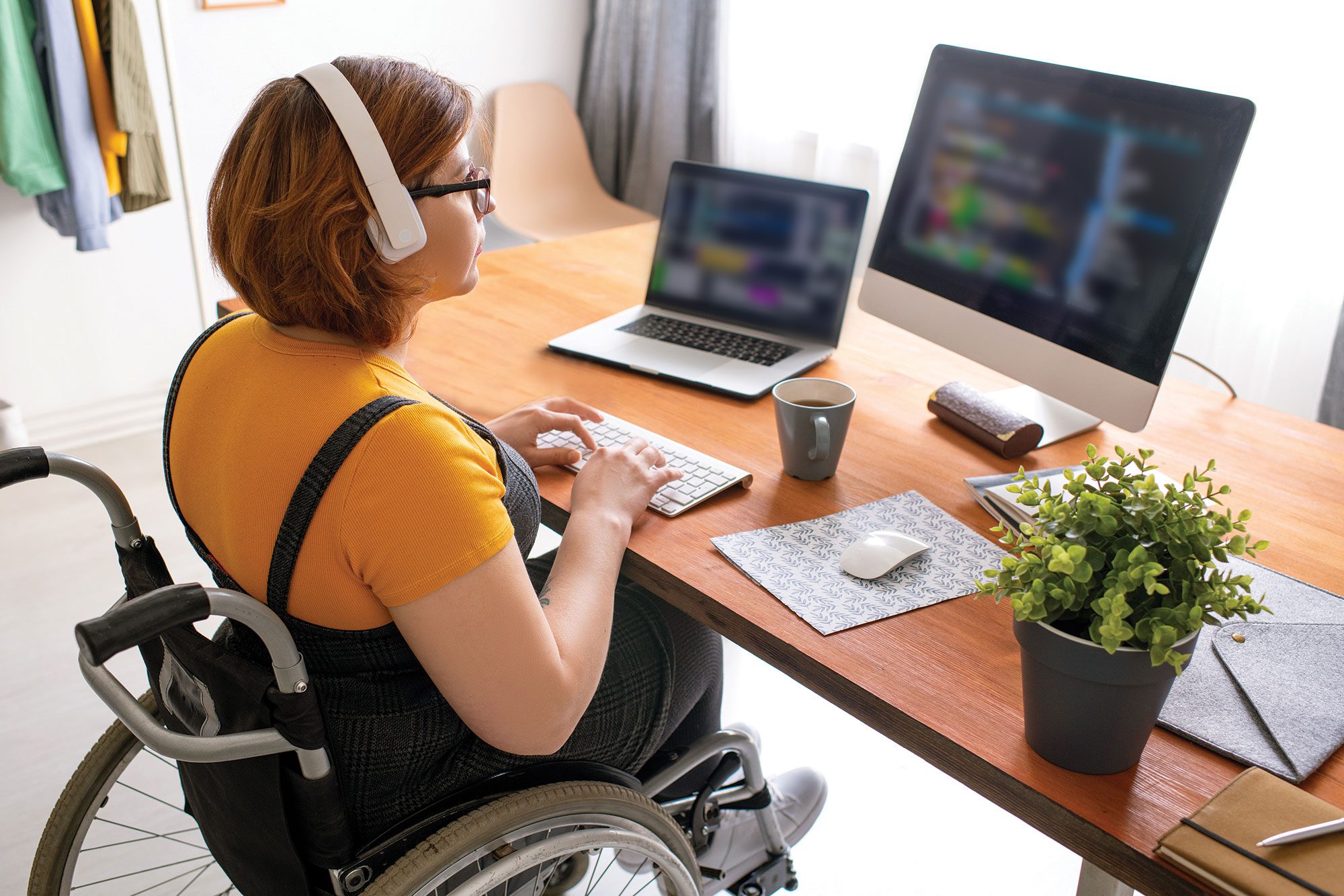 Programmiererin im Rollstuhl, die an Ihrem Laptop und PC arbeitet