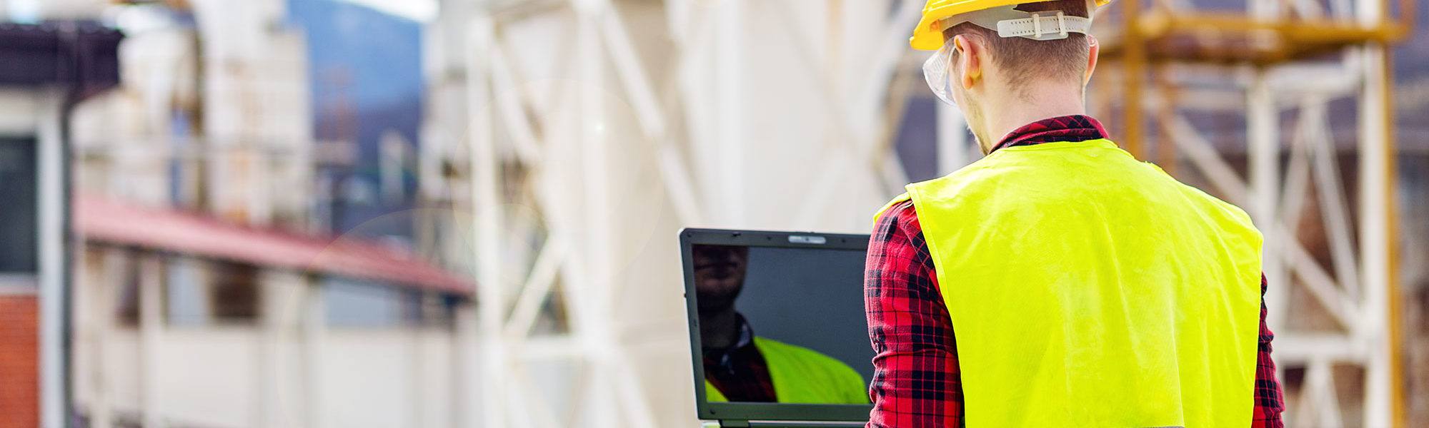 Rücken eines Arbeiters mit Schutzhelm, der auf einen Laptop schaut