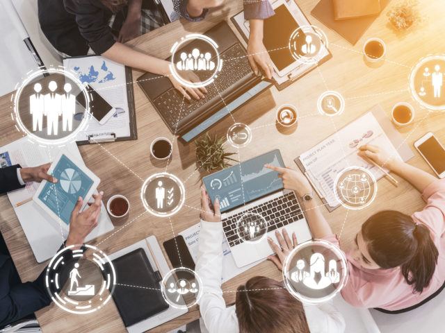 Kollegen, die an einem gemeinsamen Tisch arbeiten, und Einblendung von VR-Symbolen