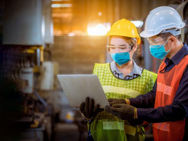 Schwerindustriearbeiter arbeiten am Laptop in der Mitte der Fabrik