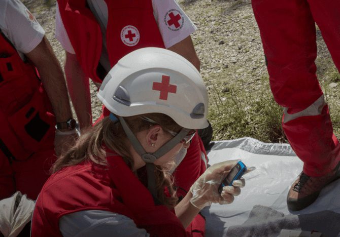 Frau mit Rotkreuz-Schutzhelm mit ihrem Mobiltelefon