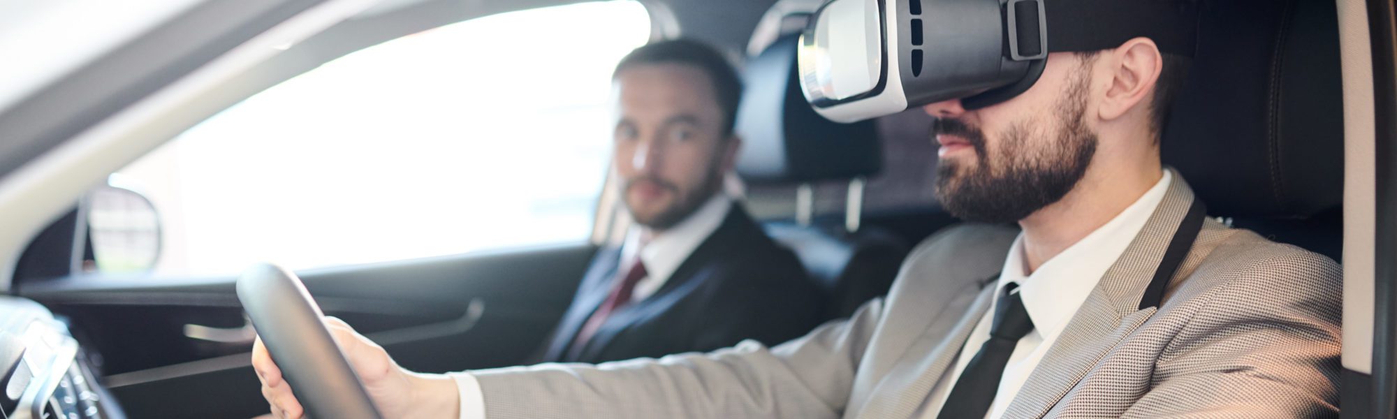Side view portrait of handsome bearded businessman wearing VR headset sitting behind wheel of luxury car, modern technology concept